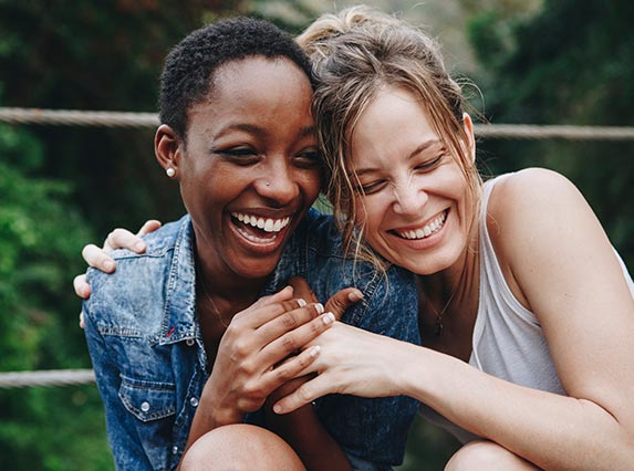 Two woman of mixed race with beautiful smiles embrace while laughing
