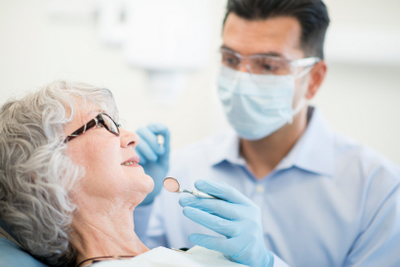Dentist wearing PPE inspecting an older female patient